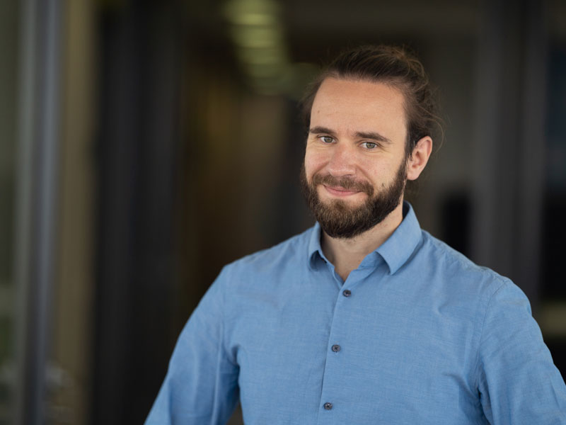 Junger Mann mit langen Haaren lächelnd im Hemd.